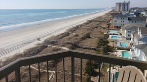 A beach view with a wooden deck, a swimming pool, and residential buildings.
