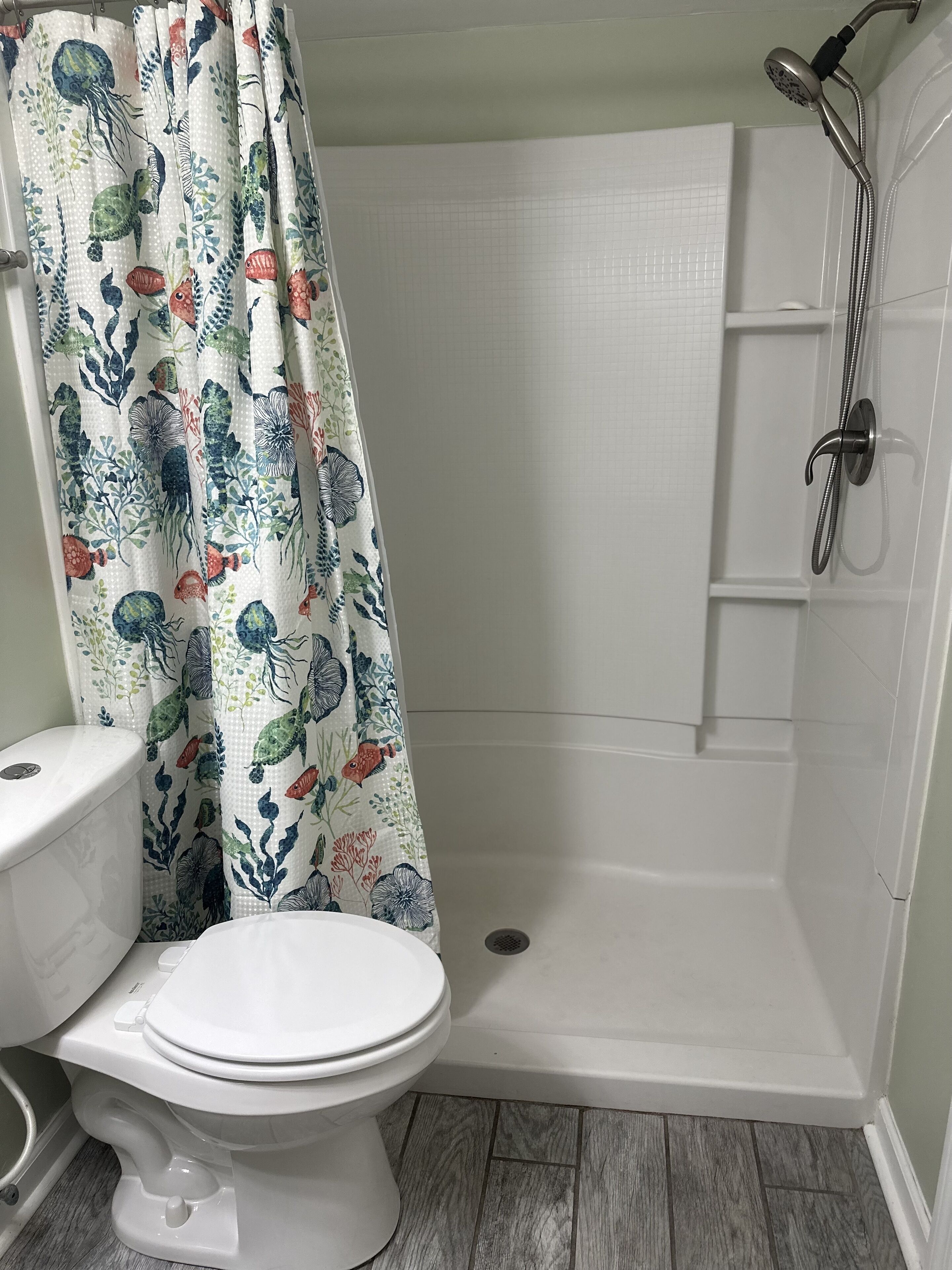 A bathroom with a shower, toilet, and a curtain with a marine theme.