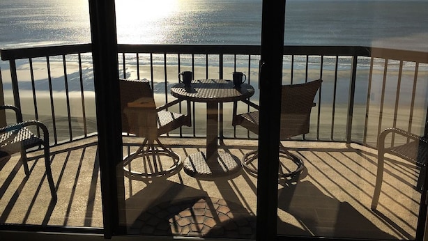 A balcony with a view of the ocean, featuring a round table and wicker chairs.
