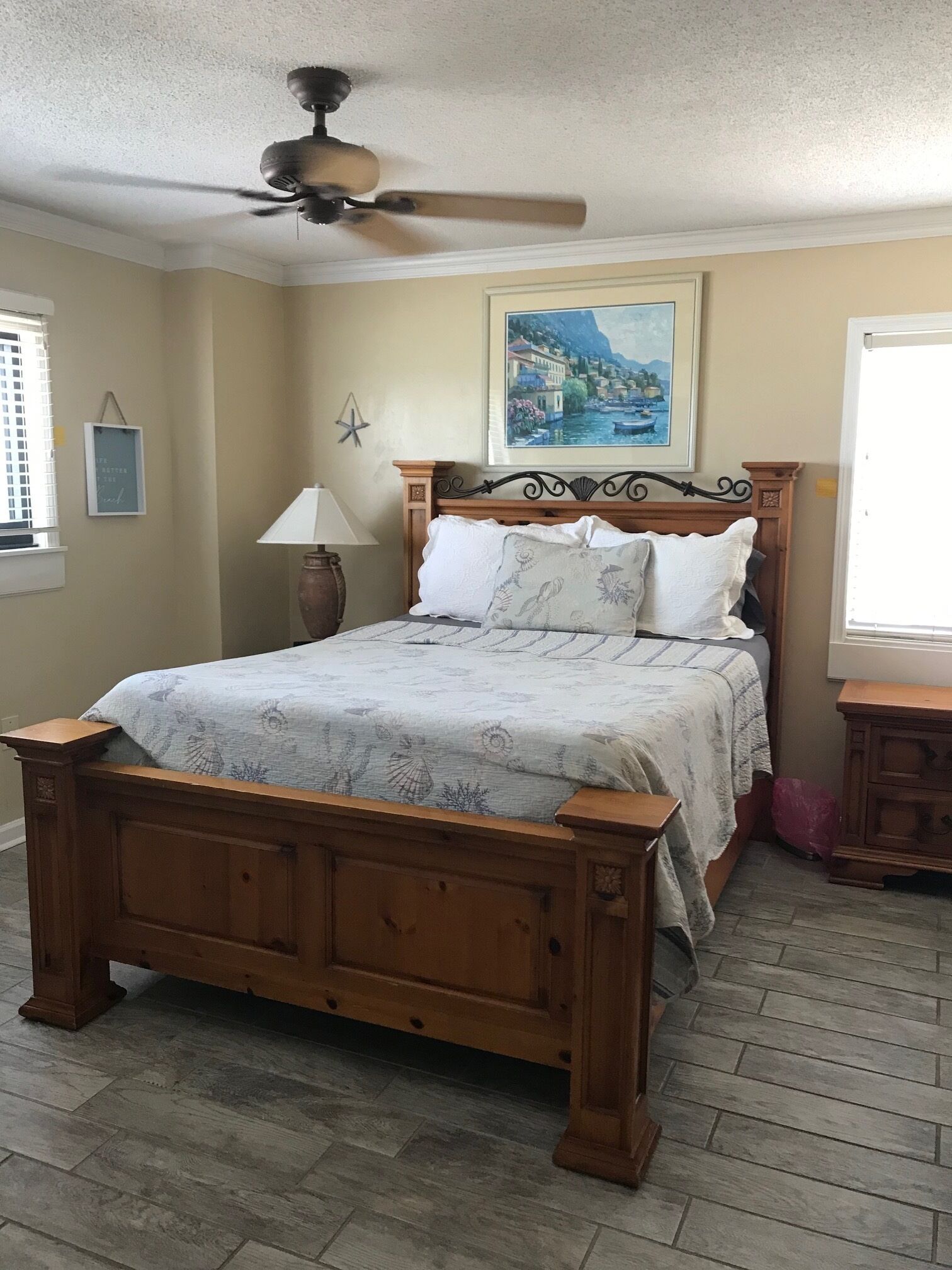 A bedroom with a wooden bed, a ceiling fan, a painting, a star decoration, and a lamp.