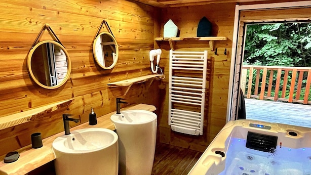 A wooden cabin bathroom with a large bathtub, two sinks, and a mirror.