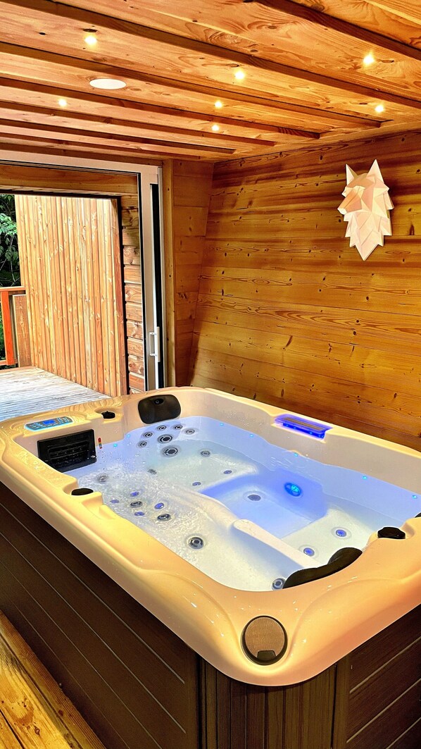 A hot tub in a wooden cabin with a wooden ceiling and walls, a window, and a door.
