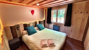 A bedroom with a wooden headboard, a bed with white linens and teal pillows, a window with curtains, and a red decorative item on the wall.