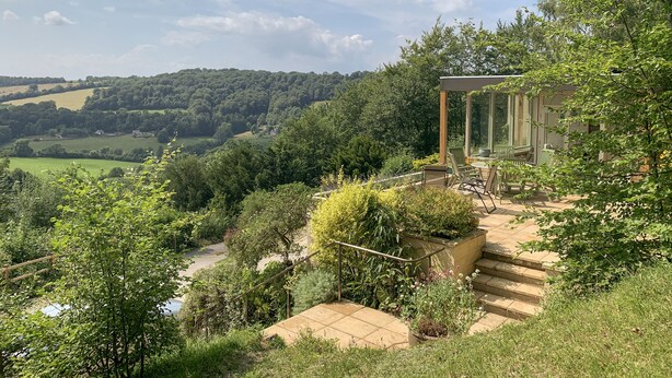 A hillside view with a glass conservatory, outdoor seating, and a stone staircase. - Under Catswood (Stroud)