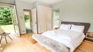 A bedroom with a large bed, wooden floor, and a bench with a fur throw. - Under Catswood (Stroud)