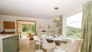 A modern kitchen with a dining area, large windows, and a view of greenery. - Under Catswood (Stroud)