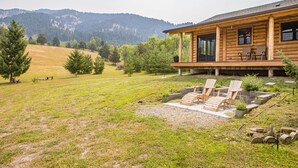 Una cabaña de madera con porche, mobiliario exterior y vistas a un paisaje montañoso.