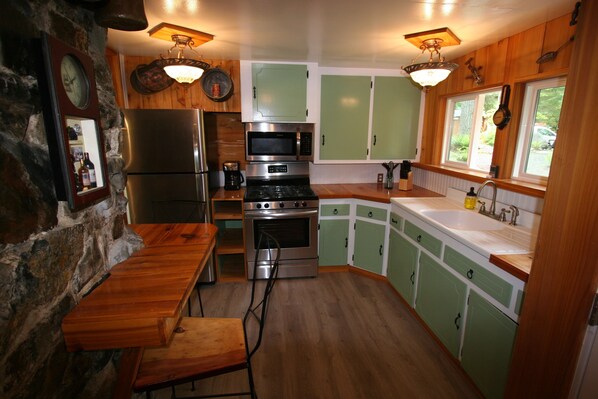 A kitchen with green cabinets, a stainless steel refrigerator, a microwave, and a stove.