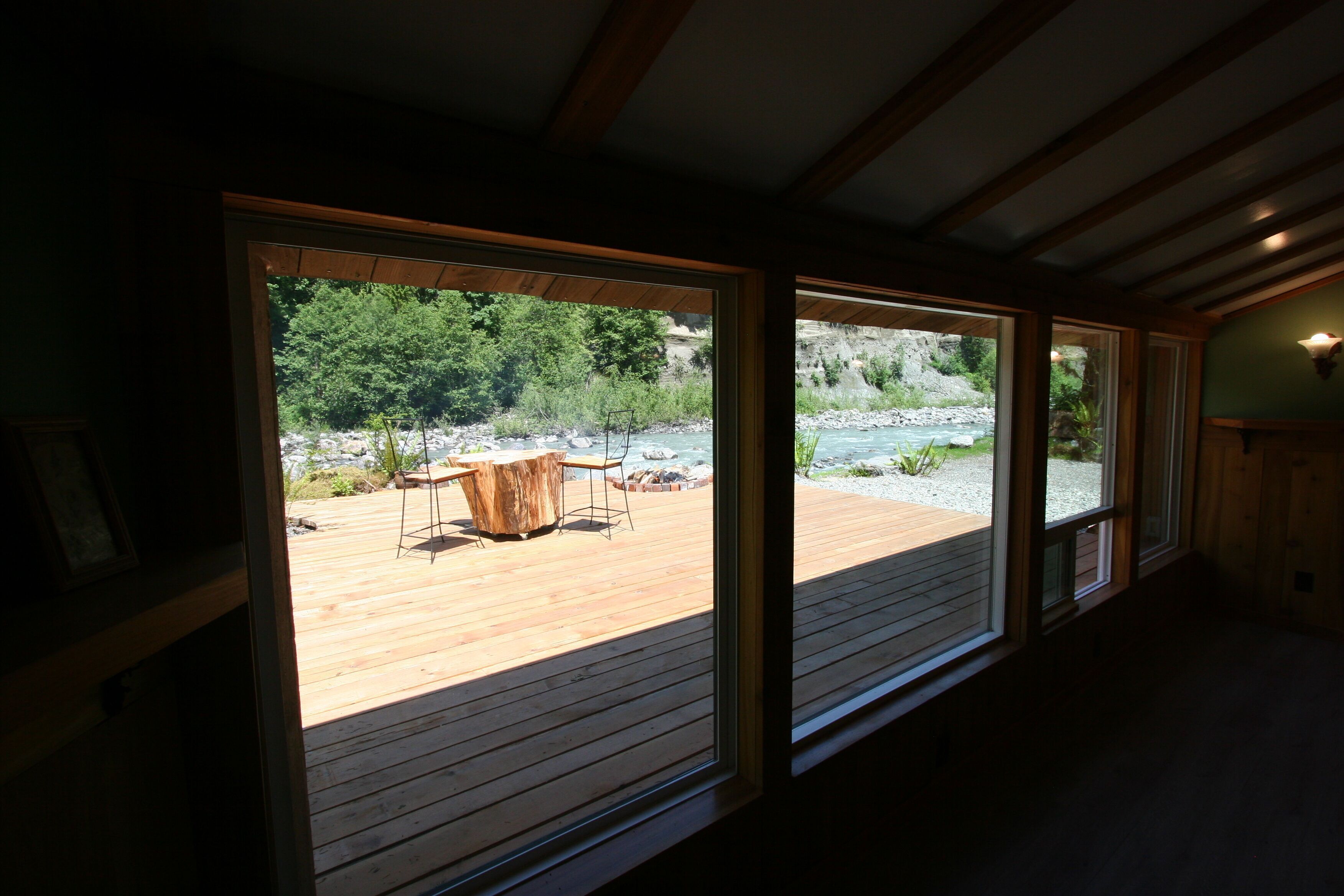 Une pièce dotée de grandes fenêtres donnant sur une terrasse en bois et un espace salon extérieur.