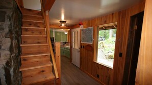 Una escalera de madera que lleva al segundo piso, una cocina con armarios verdes y una puerta que da al exterior.