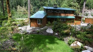 Una cabaña con techo verde, rodeada de un entorno natural de bosque.