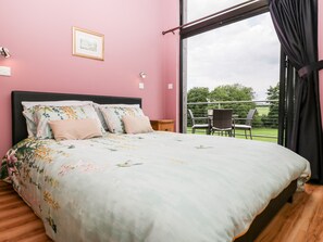 A bedroom with a bed, a window with curtains, a chair, and a small table.