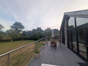 A deck with a table and chairs, surrounded by a railing, overlooking a grassy area with trees.