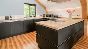Une cuisine moderne dotée d’un îlot central, de meubles de rangement aux couleurs sombres et d’une grande fenêtre qui laisse entrer la lumière naturelle.
