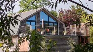 Une maison moderne en bois, dotée d’une grande baie vitrée et d’un balcon.