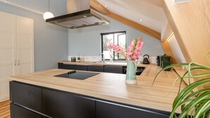 Une cuisine moderne dotée d’un plan de travail en bois, de meubles de rangement noirs, d’une hotte en acier inoxydable et d’une fenêtre laissant entrer la lumière naturelle.