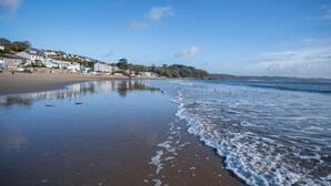 A beach with a sandy shore, a calm sea, and buildings in the background. - Ocean View - 1 Bedroom - Saundersfoot (Saundersfoot)