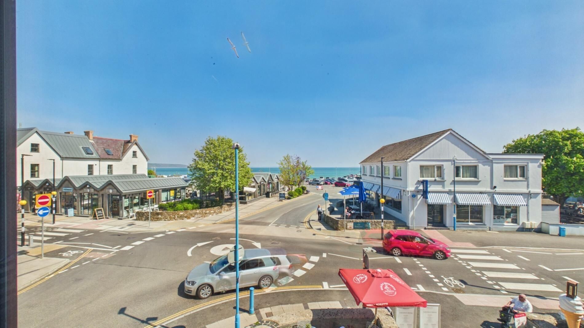 A coastal town with a road intersection, buildings, and a clear view of the sea.