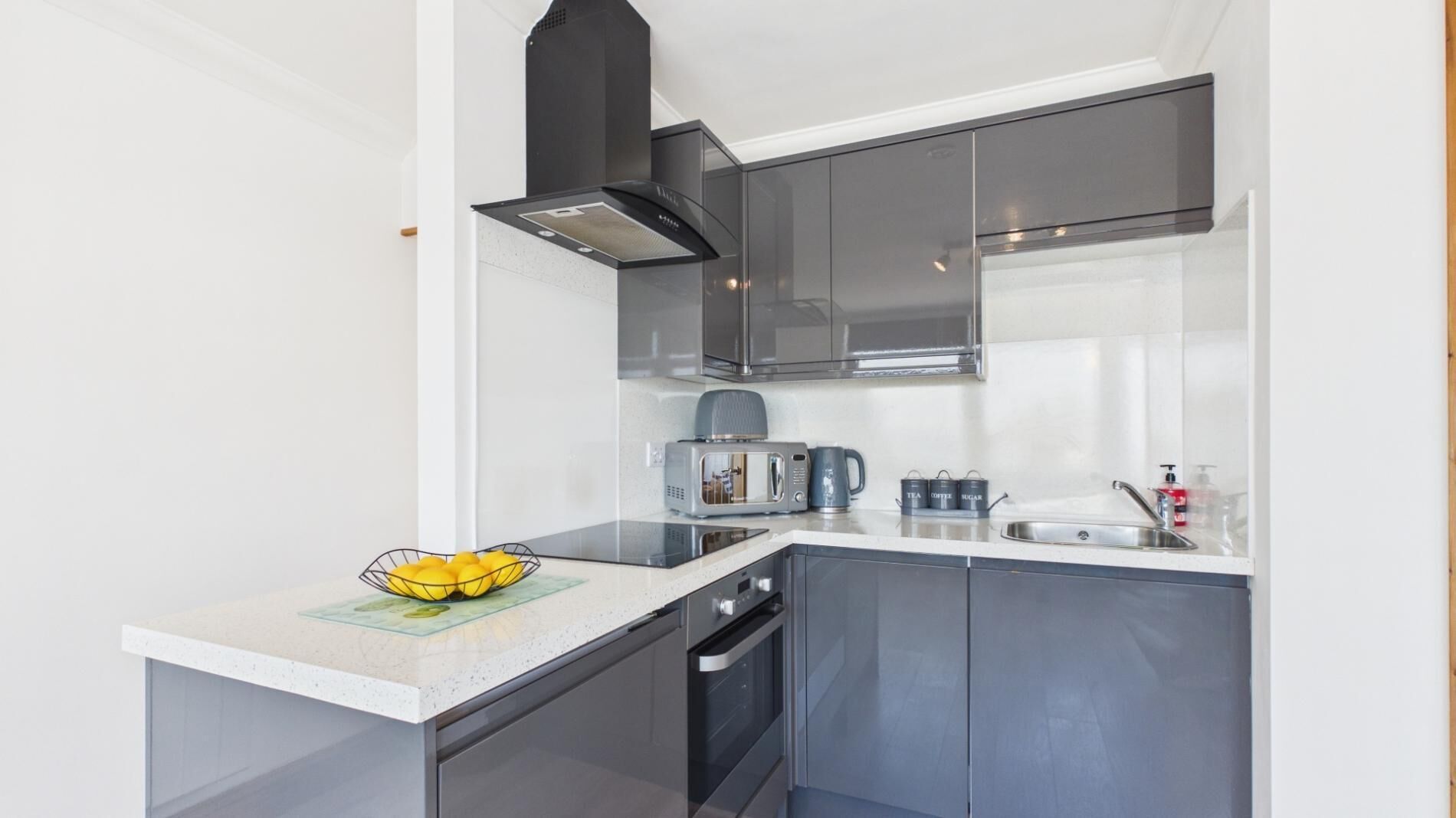 A modern kitchen with a microwave, toaster, and kettle on the counter, a stove, and a sink.