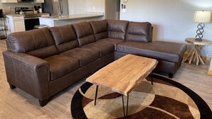 A modern living room with a brown leather sectional sofa, a wooden coffee table, and a patterned rug. - #1 Cabin~Walk to WISP! Lake access & dock! HOT Tub~Game room~Fire Pit & DOGS OK! (McHenry)