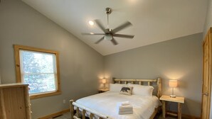 A bedroom with a wooden bed frame, a ceiling fan, two bedside lamps, a window with blinds, and a wooden nightstand. - #1 Cabin~Walk to WISP! Lake access & dock! HOT Tub~Game room~Fire Pit & DOGS OK! (McHenry)