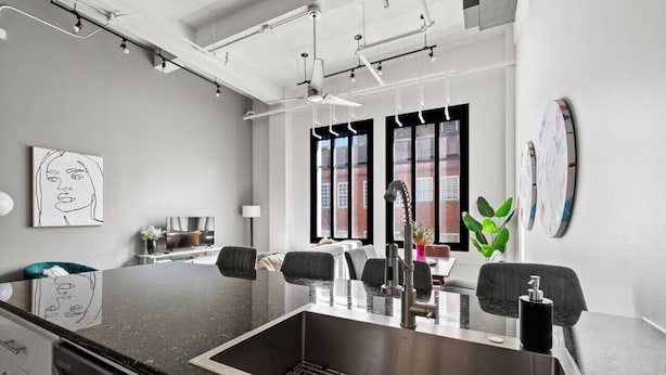 A modern kitchen with a central island, stainless steel sink, and black chairs.
