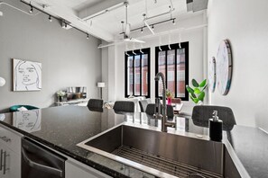 Een moderne keuken met een centraal eiland, een RVS spoelbak en zwarte stoelen.