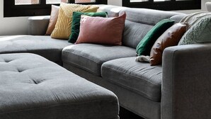 A modern living room with a sectional sofa, multiple pillows, and large windows with black frames.