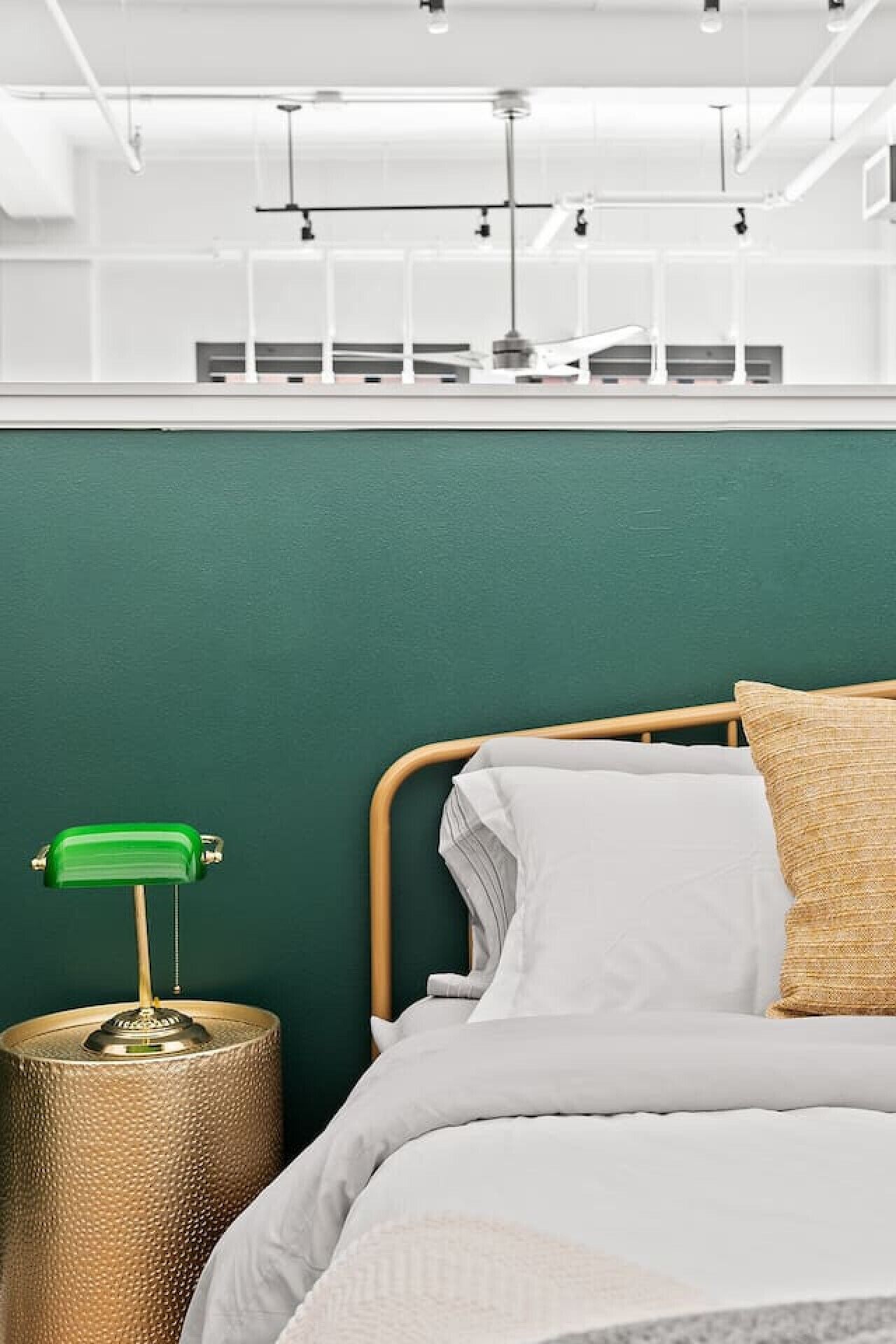 Un dormitorio con cama, pared verde, cabecera de madera, lámpara de escritorio verde y base de lámpara texturizada.