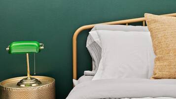 Un dormitorio con cama, pared verde, cabecera de madera, lámpara de escritorio verde y base de lámpara texturizada.