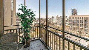 Ein Balkon mit einem Korbstuhl, einem Blumentopf und Blick auf eine Stadt mit Gebäuden.