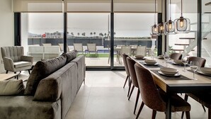 A modern dining area with a view of a pool and palm trees, featuring a long table with chairs and a sofa. - Modern villa with private pool (Mar de Cristal)