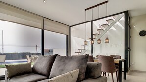 A modern living room with a grey sofa, dining area with chairs and a table, and large windows offering a view. - Modern villa with private pool (Mar de Cristal)