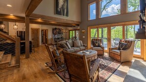 Un salon spacieux avec un plafond haut, des poutres en bois, un grand tableau et une vue sur l’extérieur.