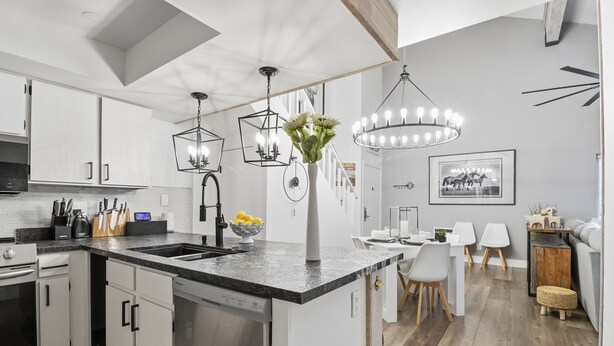 A modern kitchen with white cabinets, a black countertop, and a central island. There are pendant lights above the island and a chandelier in the dining area. - JUST FINISHED RENOVATIONS 2023!!! A lavishly styled ski-in/out winter escape! (Brian Head)