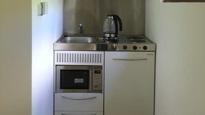 A compact kitchen with a built-in oven, microwave, and stovetop, featuring white cabinets and a window above the sink. - Highgate Studio (London)