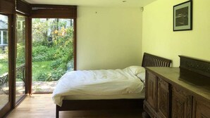 A bedroom with a bed, a wooden dresser, a framed picture on the wall, and a sliding glass door leading to a garden. - Highgate Studio (London)
