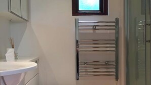 A modern bathroom with a toilet, a small window, and a glass shower enclosure. - Highgate Studio (London)