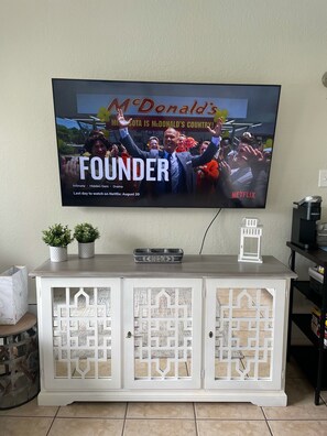 A television displaying 'The Founder' on Netflix, mounted on a wall above a white cabinet with decorative cutouts.