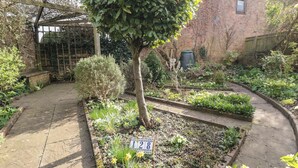 A garden with a variety of plants and a brick building in the background. - Wren's Nest (Thirsk)