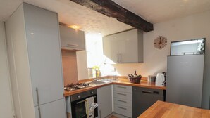A compact kitchen with a gas stove, a built-in oven, a refrigerator, and a wooden dining table. - Wren's Nest (Thirsk)
