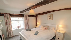 A bedroom with a bed, nightstands, a window with curtains, and a wooden ceiling beam. - Wren's Nest (Thirsk)
