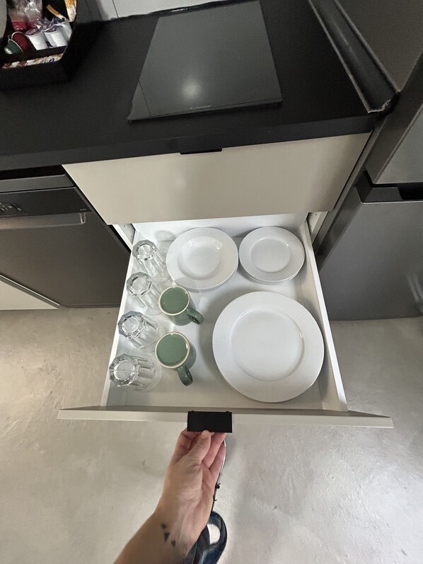 A kitchen drawer with white plates, green mugs, and clear glasses.