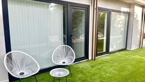 A modern building with large sliding glass doors, two white chairs, and a well-maintained lawn.
