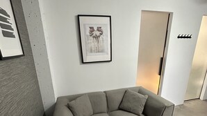 A modern living room with a grey sectional sofa, a small round table, and a framed artwork on the wall.