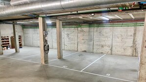 A parking garage with concrete floors and walls, marked parking spaces, and visible ductwork on the ceiling.