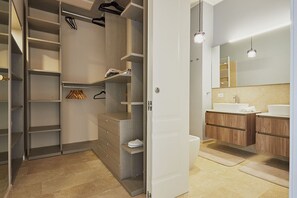 A modern bathroom with a large mirror, two sinks, and a walk-in closet with shelves and hanging space.