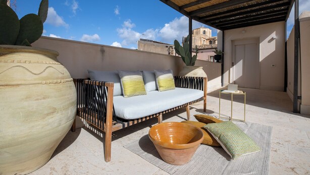 Una terraza en la azotea con un sofá, una maceta de terracota grande y una planta de cactus.