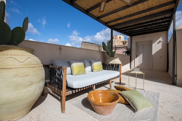 A rooftop terrace with a sofa, a large terracotta pot, and a cactus plant.