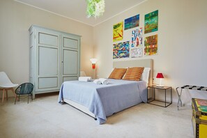 Un dormitorio con cama, armario, silla, mesita de noche con lámpara y una obra de arte en la pared.